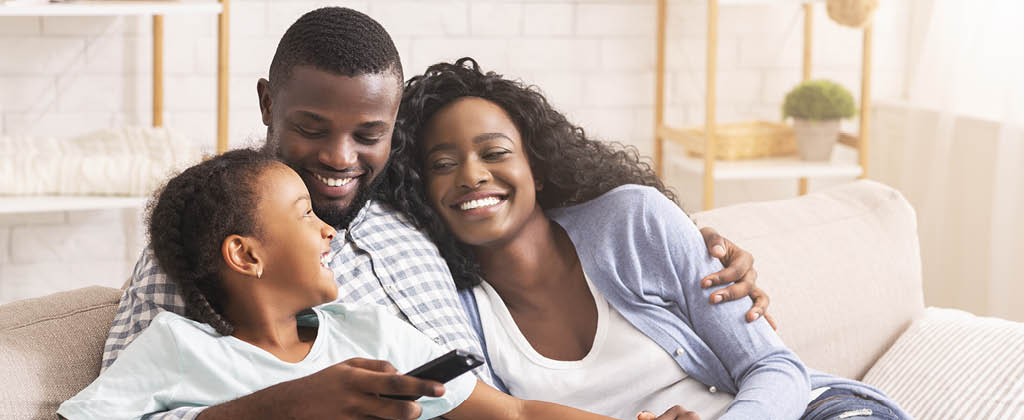 Smiling african american family relaxing on couch and watching TV at home, man switching channels